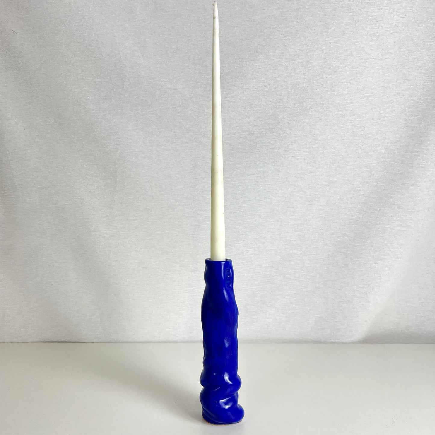 Blue candle holder with a white candle on a gray background