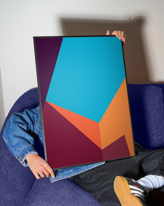 Person holding a colorful geometric abstract poster on a white wall.