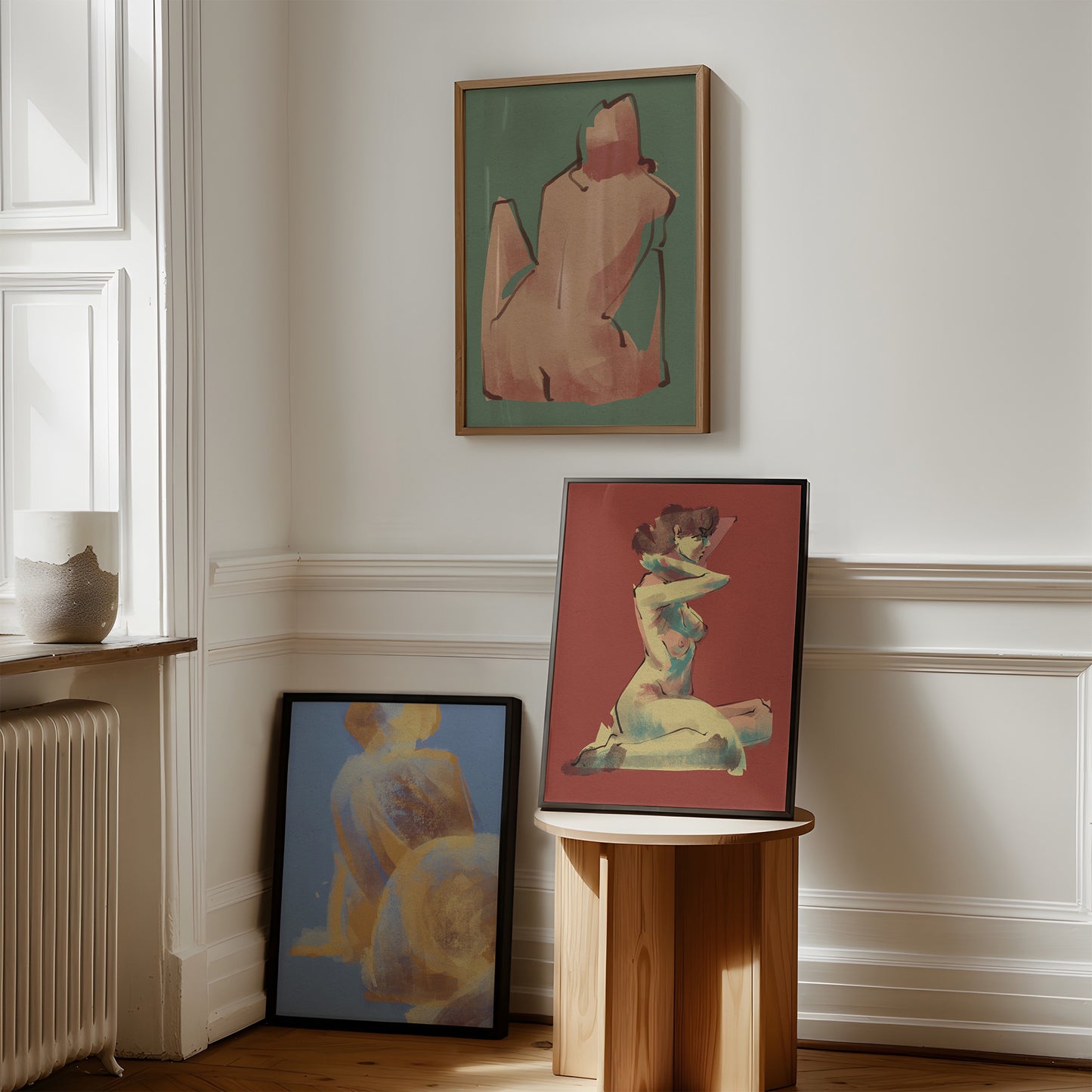 Three framed artworks with stylized figures of women on a wall in a room with wooden floor