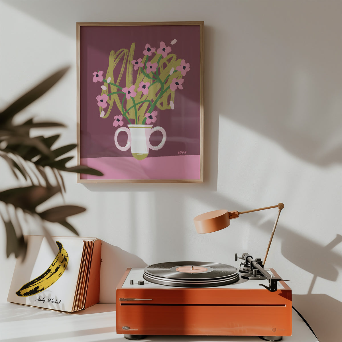 Orange record player on a white surface with a framed artwork of flowers on the wall.