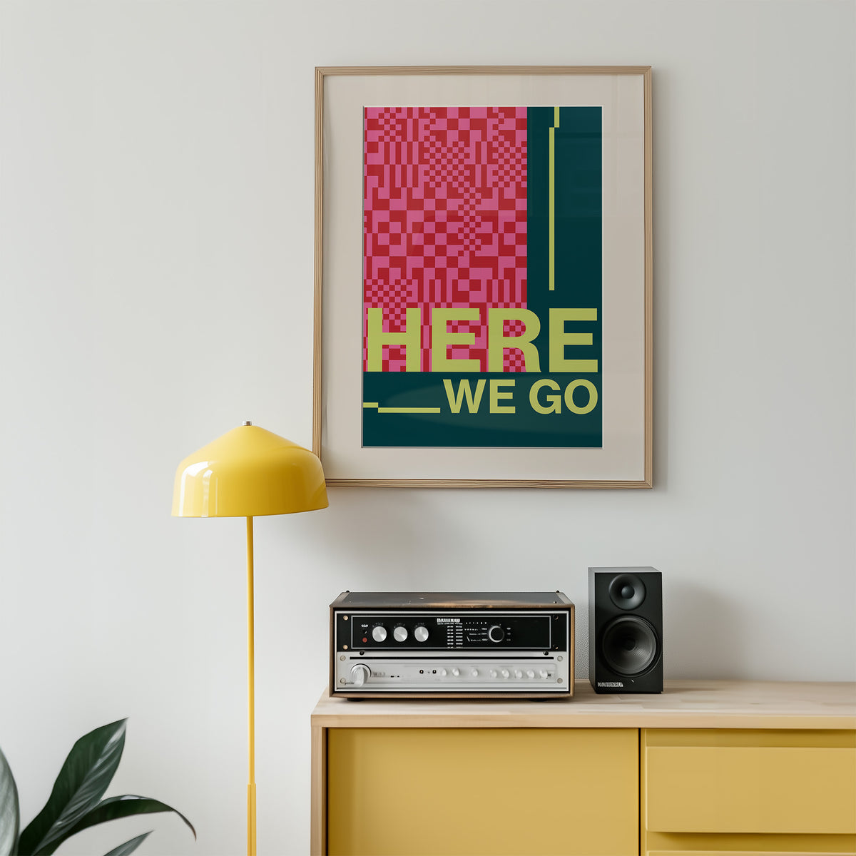 Framed poster with 'HERE WE GO' text on a wall above a yellow cabinet with audio equipment.