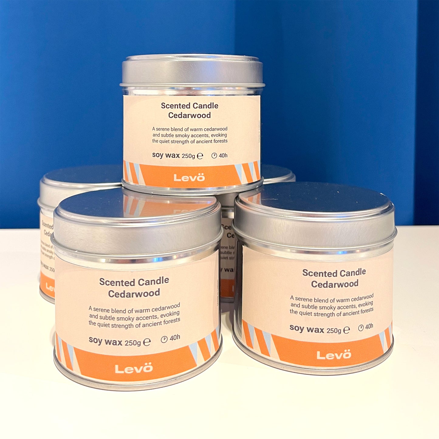 Four tins of Levö Cedarwood scented candles on a white surface with a blue background