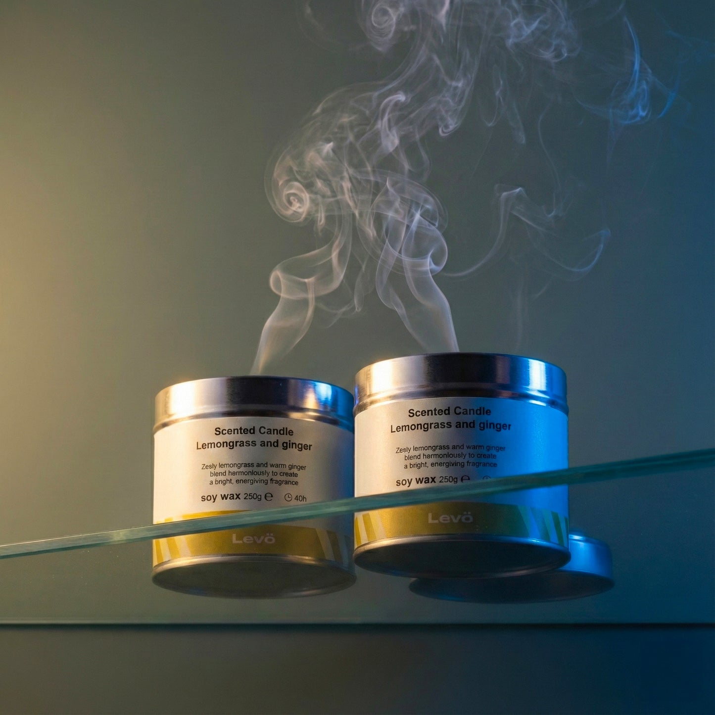 Two scented candles by Levo with smoke rising from them on a reflective surface.
