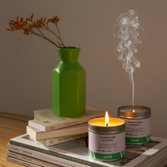 Candle with smoke, green vase, and books on a wooden surface