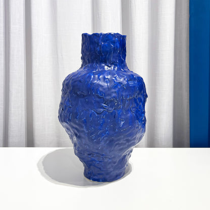 Blue textured vase on a white surface with a white curtain background by Anna De at Levö