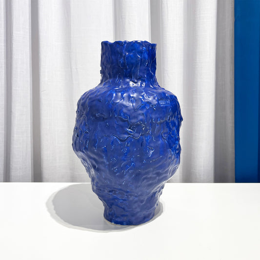 Blue textured vase on a white surface with a white curtain background by Anna De at Levö