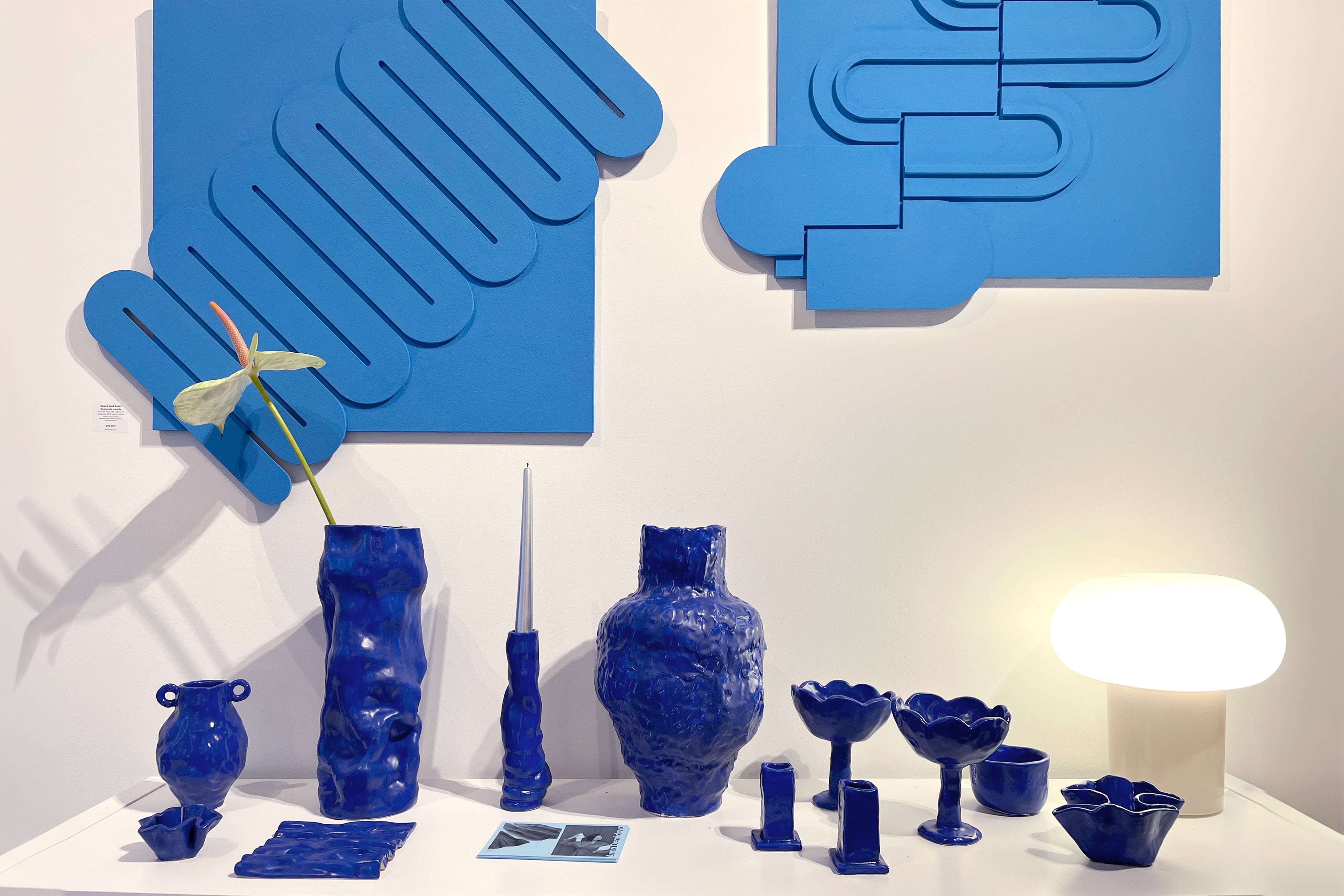 Collection of blue ceramic vases and decorative items on a white surface with abstract blue wall art.