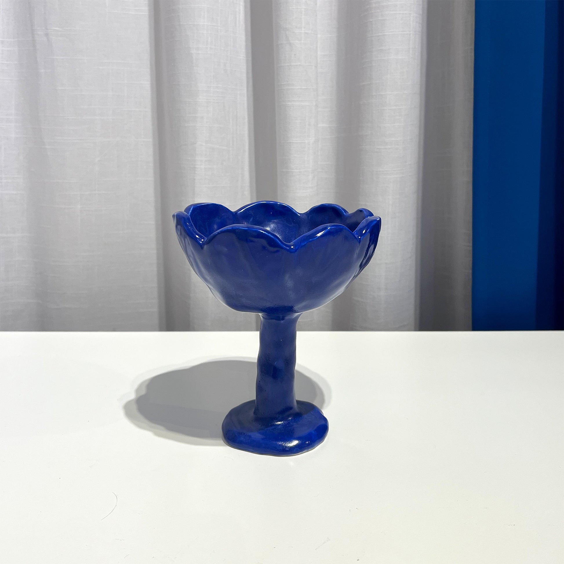 Blue glass bowl by Anna Demidova Levö  on a white surface with a light gray curtain background