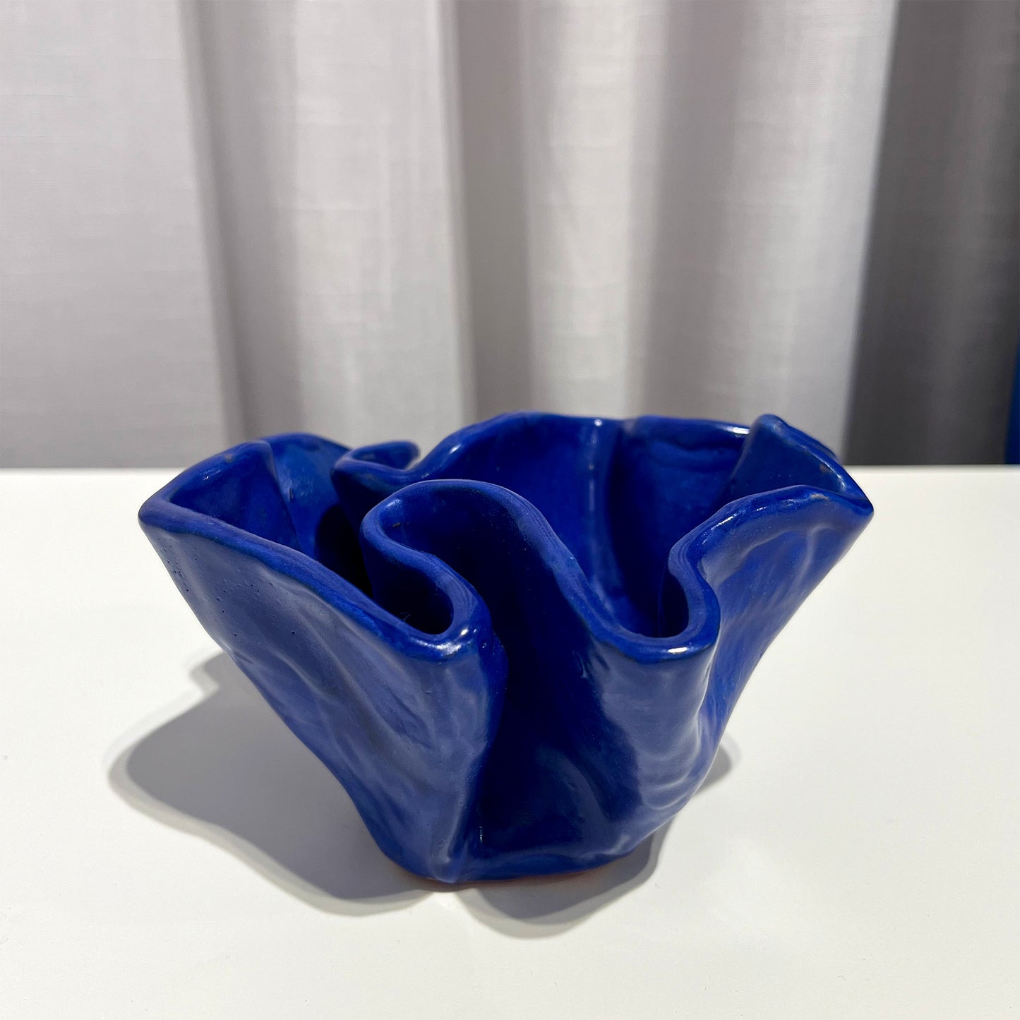 Blue ceramic bowl by Anna Demidova Levö on a white surface with a white curtain background