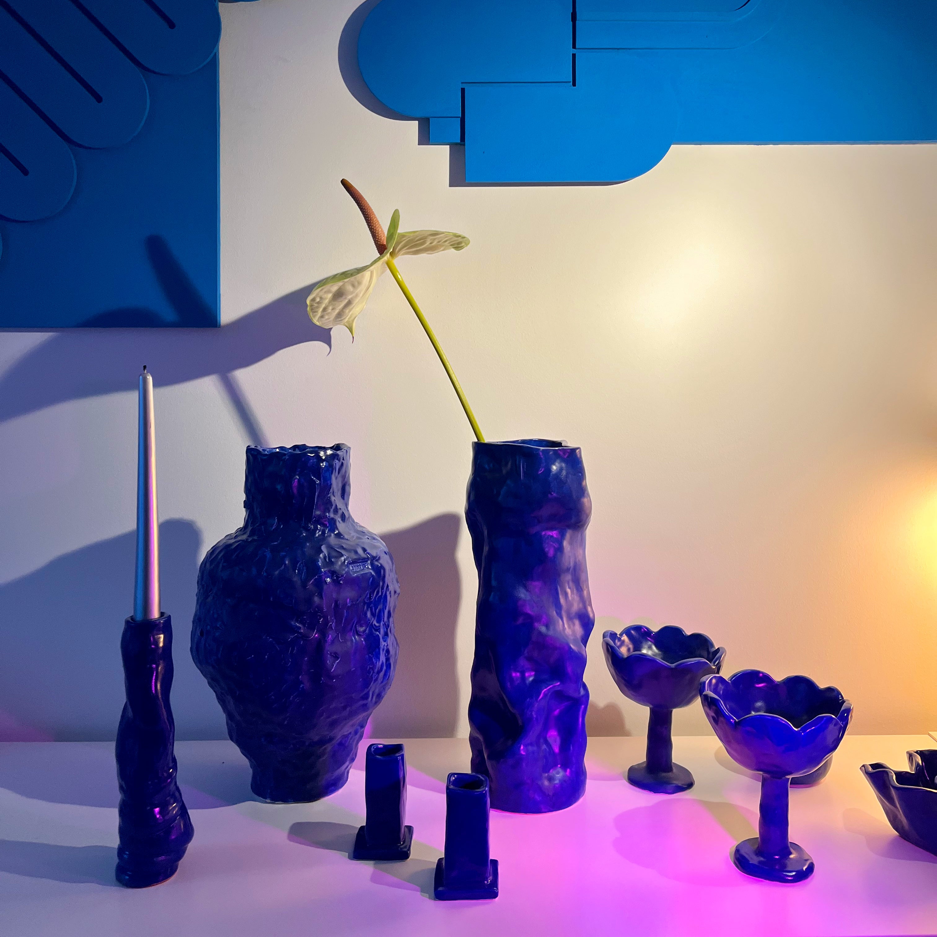 Set of blue ceramic vases and decorative items against a white wall with blue abstract art.