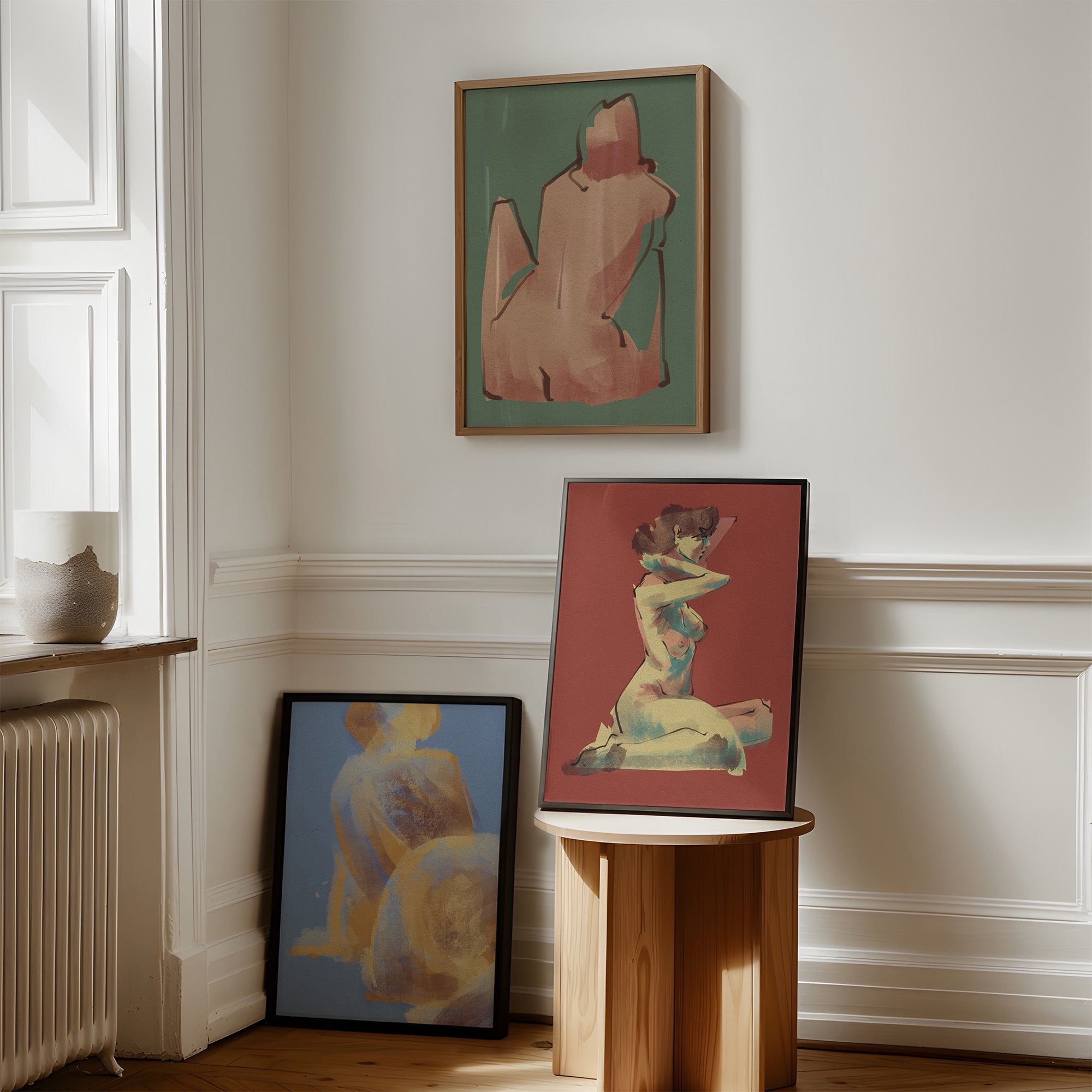 Three framed artworks with stylized figures of women on a wall in a room with wooden floor