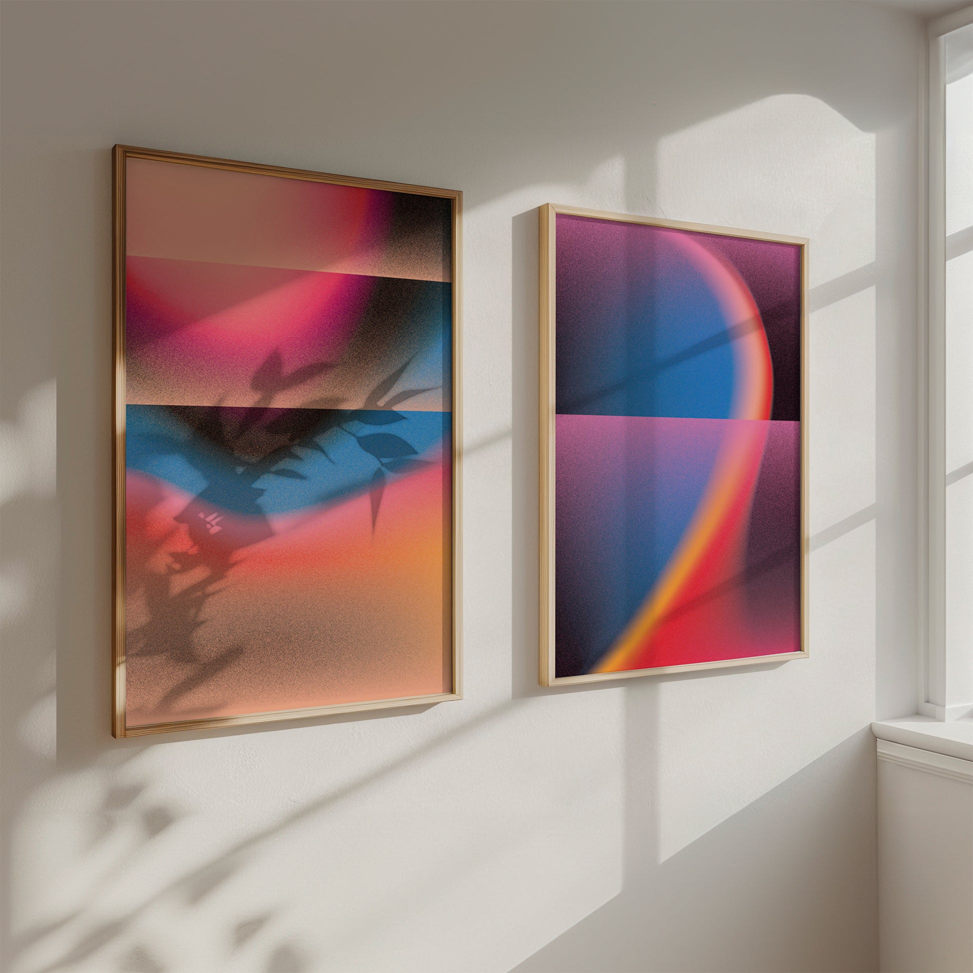 Two abstract art pieces in wooden frames on a white wall with sunlight casting shadows.