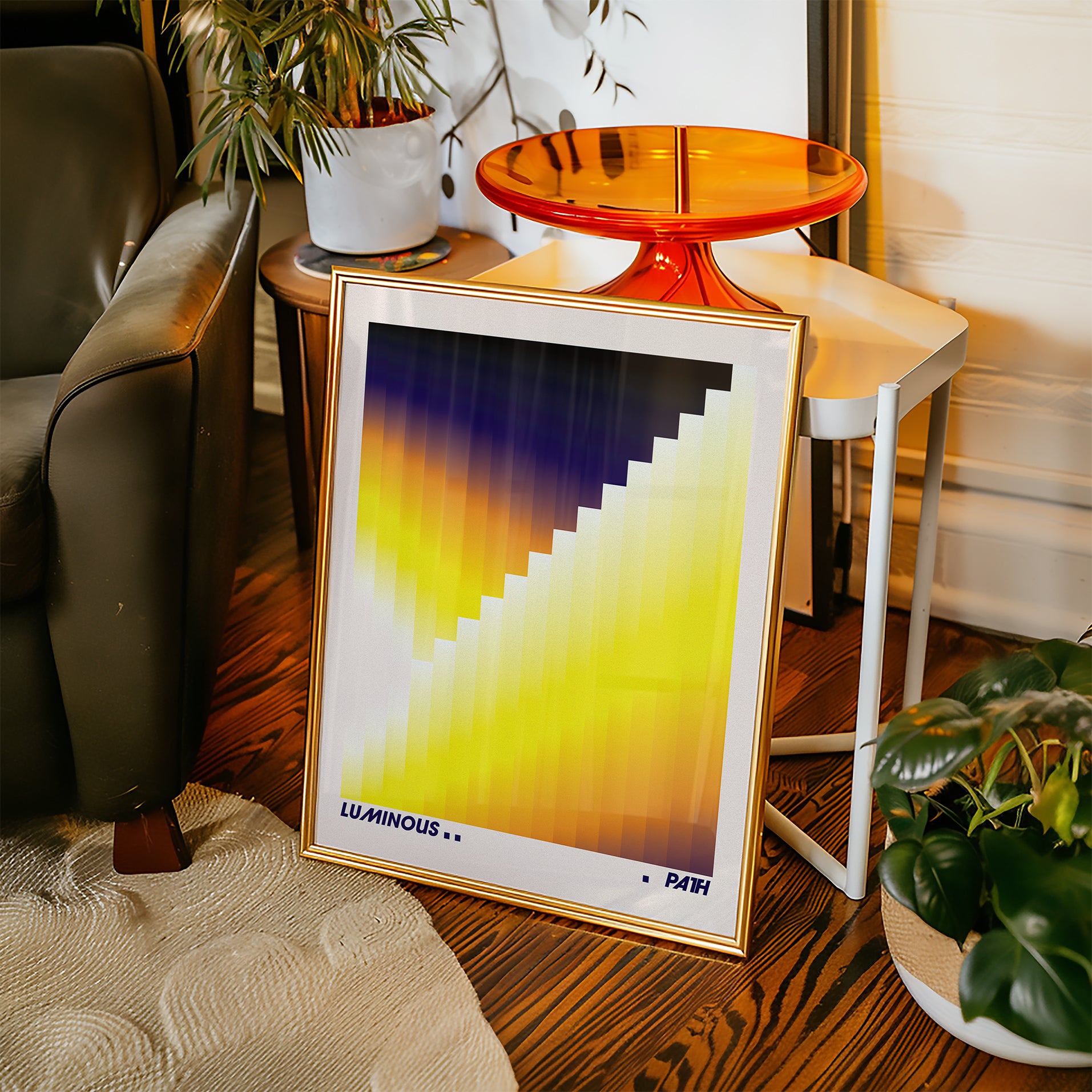 Framed abstract art print on a wooden floor with a chair and plants in the background