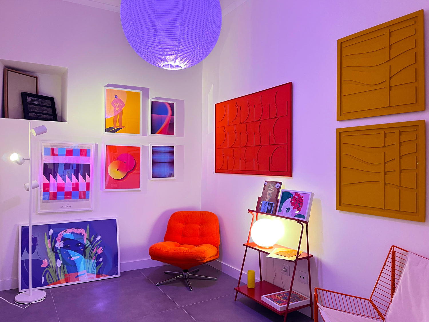 Modern studio of posters in Lisbon with colorful artwork, a red chair, and a purple ceiling light.